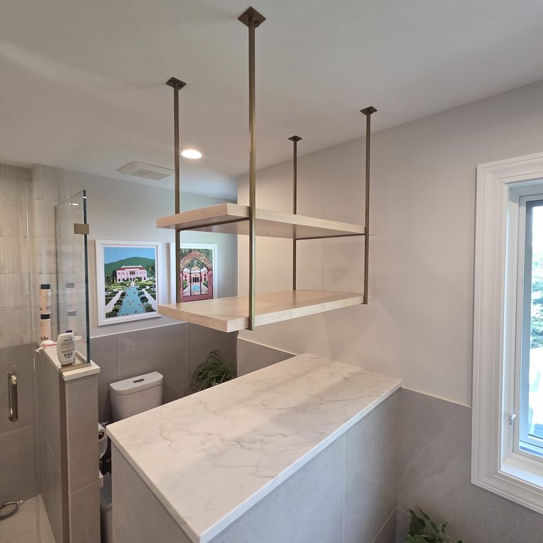 Bathroom with a glass shower, a capped half wall and open shelves suspended from the ceiling by MDR Design-Build-Remodel