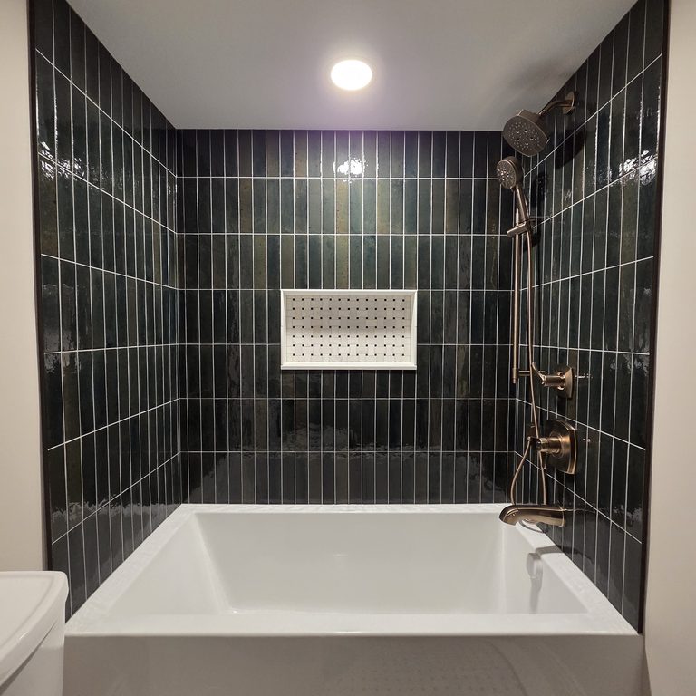 Bathroom with deep green vertical tile around a soaking tub and brushed-gold fixtures by MDR Design-Build-Remodel