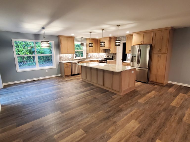 Open kitchen with natural maple shaker cabinets, a large island and wood-look plank floors by MDR Design-Build-Remodel